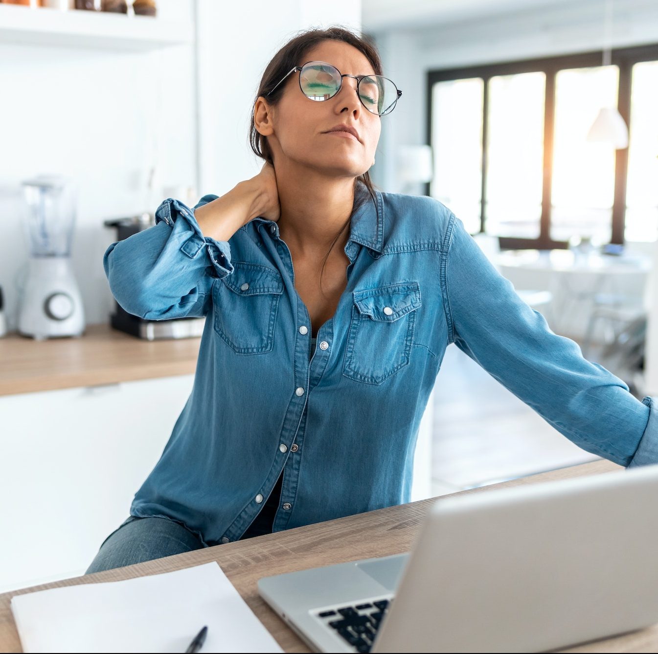 Tired business woman with neck pain looking uncomfortable while working from home on laptop.